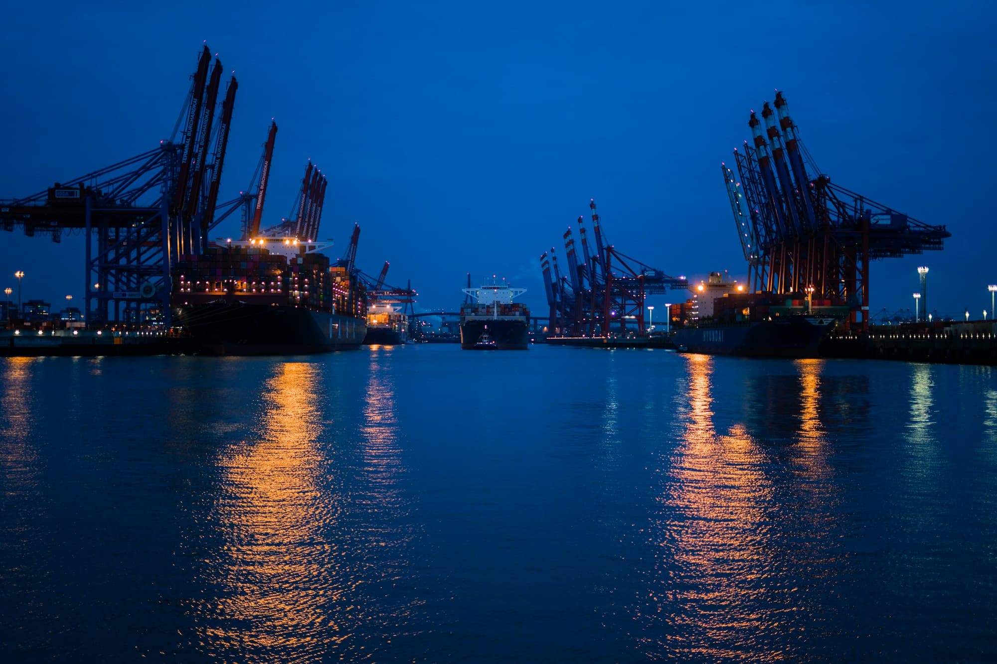 Hamburger Hafen mit beleuchteten Containerbrücken am Abend